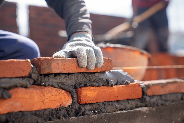 bricklayer-industrial-worker-installing-brick-masonry-with-trowel-putty-knife-at-construction-site